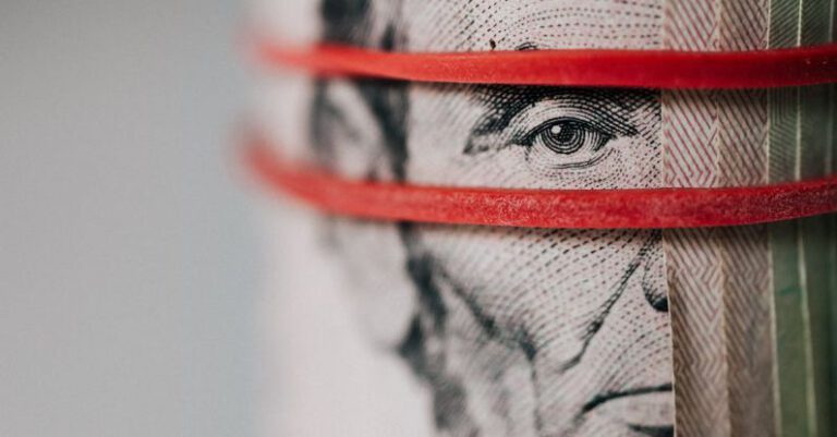 Exchanges - Closeup of rolled United States five dollar bills tightened with red rubber band